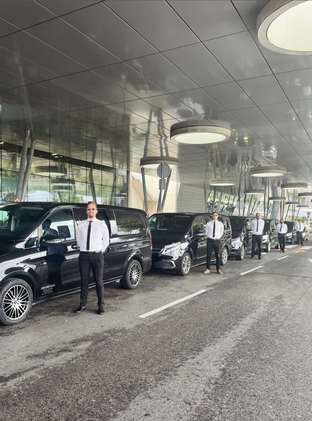 Chauffeurs standing beside a line of black Mercedes-Benz V-Class vans at Dubrovnik Airport, ready for private airport transfers